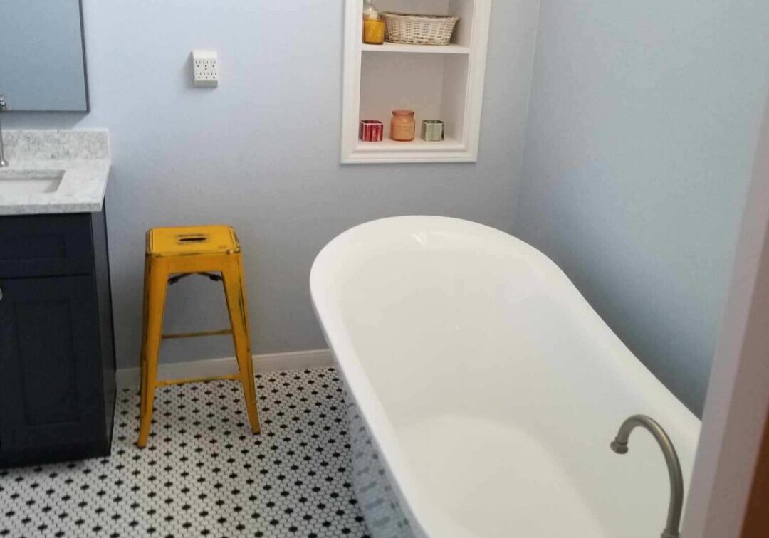 A bathroom with black and white tile and a yellow stool.